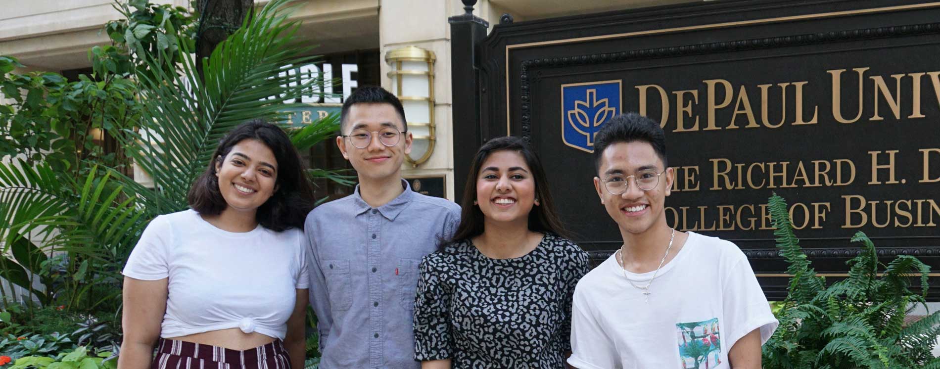 Four friends stand smiling in front of DePaul's College of business sign