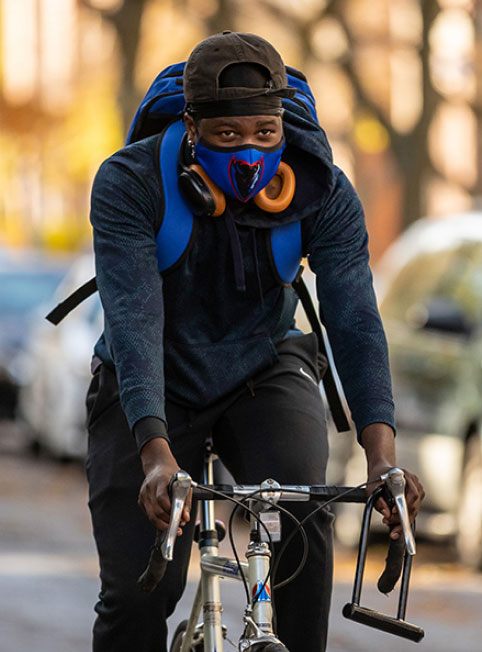 A man cycles in he city, wearing a medical mask. 