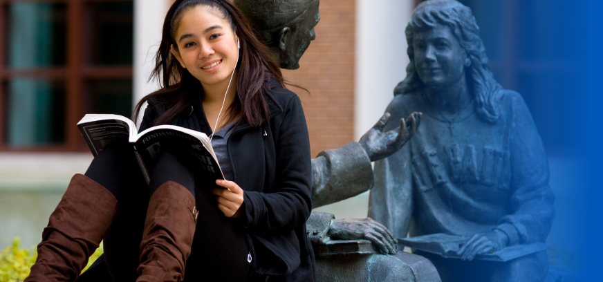 A young woman reading a book near a statue of a man and woman