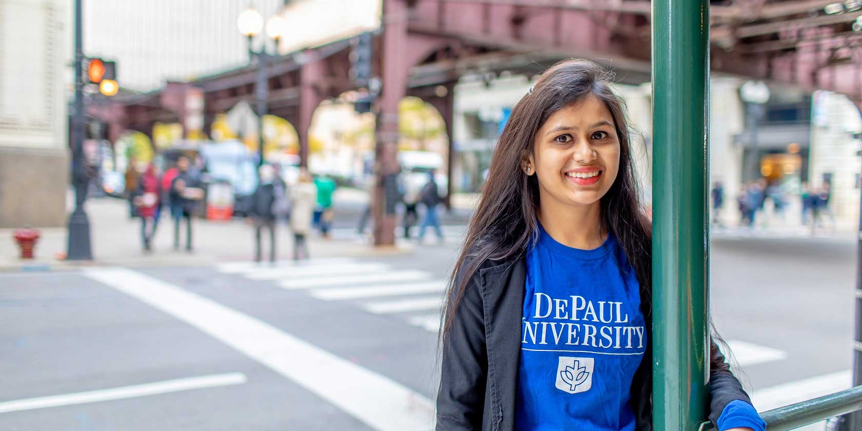 A smiling young woman with long dark hair wearing a DePaul t-shirt.

